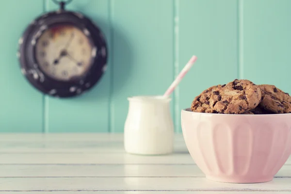 Pink bowl with chocolate chip cookies, a watch and a glass of milk. Robin egg blue background. Vintage look.