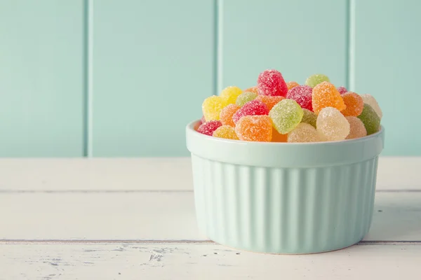 Colorful sweet jellies with sugar in a turquoise classic whiteware baking bowl on a white wooden table with a robin egg blue background. Vintage look.