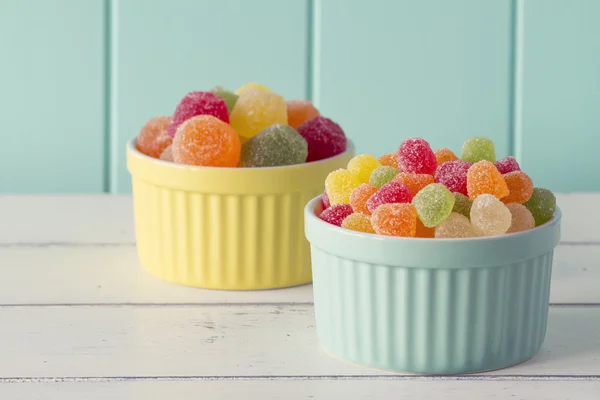 Colorful sweet jellies with sugar in two yellow and turquoise classic whiteware baking bowls on a white wooden table with a robin egg blue background. Vintage look.