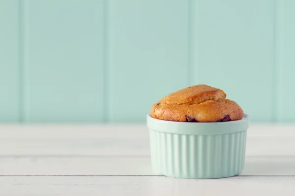 A turquoise classic whiteware baking bowl with a muffins on a white wooden table with a robin egg blue background. Vintage look.