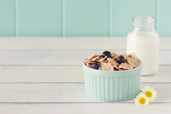 A turquoise classic whiteware baking bowl  with cereals and blueberries and a school milk bottle on a white wooden table with a robin egg blue background. Vintage.