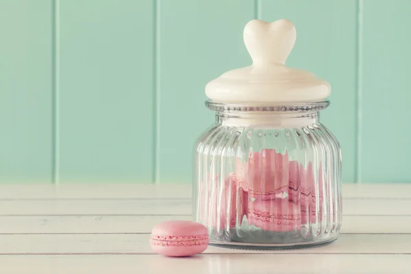 Some delicious pink macarons in a glass jar on a white wooden table with a robin egg blue background. Vintage Style.