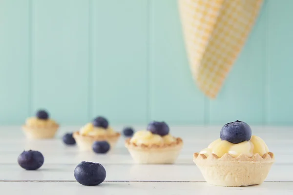 Tartlets with blueberries and pastry cream on a white wooden table with a robin egg blue background and a yellow checkered napkin. Vintage Style.