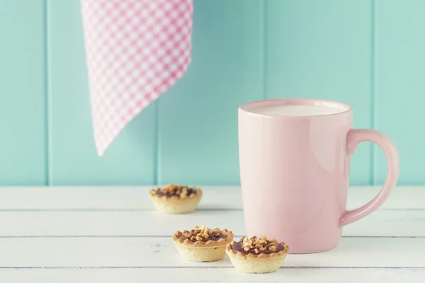 Some delicious tartlets with nutella and almonds and a mug of milk on an old white wooden table with a robin egg blue background. Vintage Style.