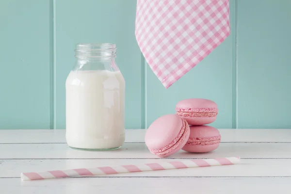 Some pink macarons and a school milk bottle on an old white wooden table with a robin egg blue background. Vintage Style.
