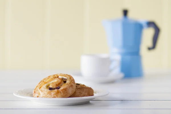 Puff pastry spirals with coffee and a steel moka pot on a white wooden table with a yellow wainscot. Vintage Style.