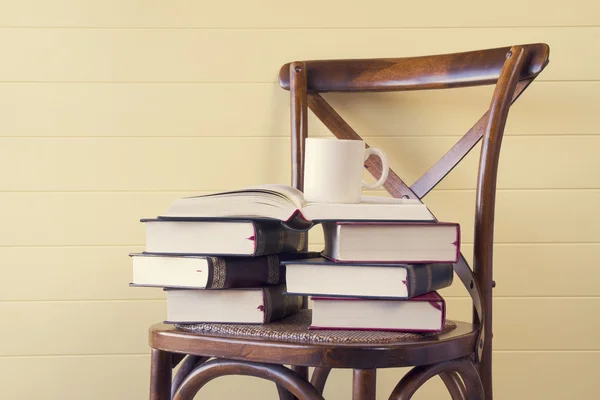 A stack of books and an mug on a chair. In the background, a yellow wainscot. Back to school. Vintage Style.