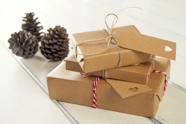 Some paper parcels wrapped tied with tags. Christmas gift boxes wrapped with paper kraft and tied with red & white baker\'s twine on a white wooden table. Vintage Style.