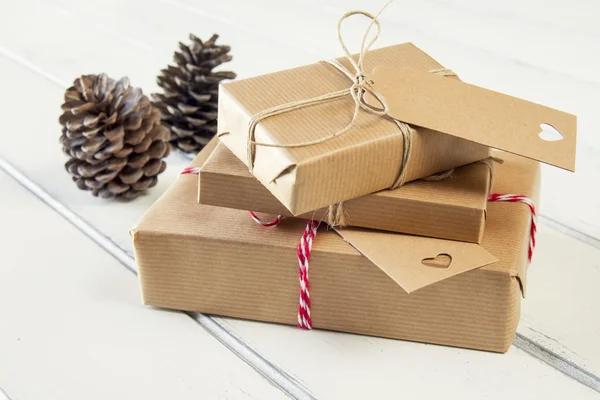 Some paper parcels wrapped tied with tags. Christmas gift boxes wrapped with paper kraft and tied with red & white baker's twine on a white wooden table. Vintage Style.