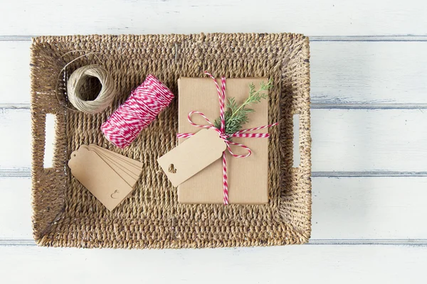 A paper parcel with a pine branch, wrapped tied with a tag on a tray. Christmas gift boxe wrapped with paper kraft and tied with red & white baker's twine on a white wooden table. Vintage Style.