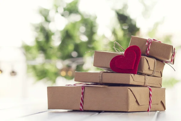 Some paper parcels wrapped tied with a tag. A red heart on a gift box wrapped with paper kraft and tied with red & white baker's twine on a white wooden table. Vintage Style.