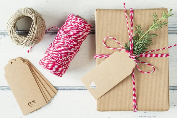 A paper parcel with a pine branch, wrapped tied with a tag. Christmas gift boxe wrapped with paper kraft and tied with red & white baker\'s twine on a white wooden table. Vintage Style.