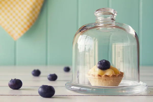 Tartlet with blueberries and pastry cream on a glass bell jar