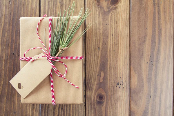 A paper parcel wrapped tied with a tag. A christmas gift box wrapped with paper kraft and tied with red & white baker\'s twine on a wooden table. Vintage Style.