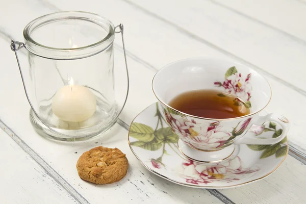 A tea cup with a candle and a shortbread on a white wooden table. Vintage Style.