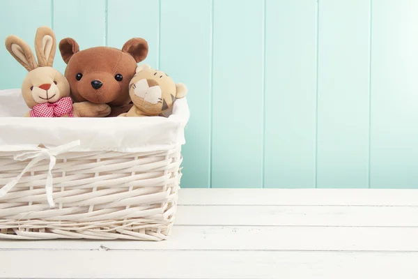 Stuffed animal toys in a basket on the floor. A turquoise wainscot.
