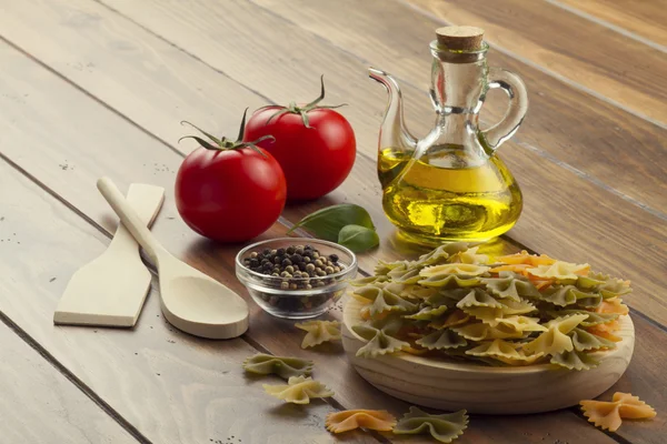 Some ingredients in a wooden table for cooking Italian pasta: tomatoes, farfalle, olive oil, peppermint and pepper