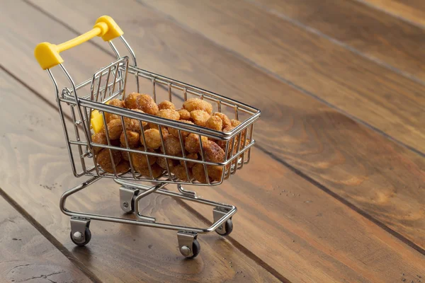 Some honey roasted peanuts in a shopping cart on a wooden table. Commerce, shop and supermarket concept.