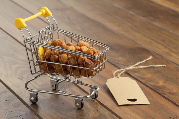 Some honey roasted peanuts in a shopping cart and a tag on a wooden table. Commerce, shop and supermarket concept.