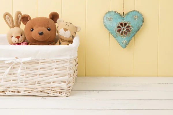 Stuffed animal toys in a basket on the floor and a blue heart on the wainscot.