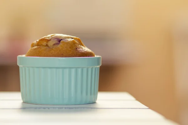 A muffin in a blue classic whiteware baking bowl on a white wooden table.