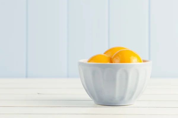 Some canned peaches in a blue bowl on a white wooden table