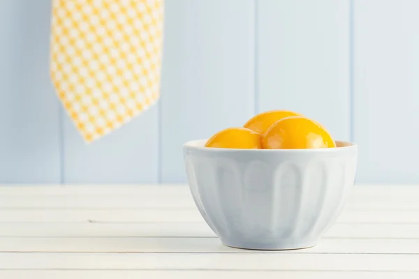 Some canned peaches in a blue bowl on a white wooden table