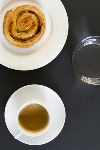 Breakfast: a coffee, a danish puff pastry swirl and a glass of water.