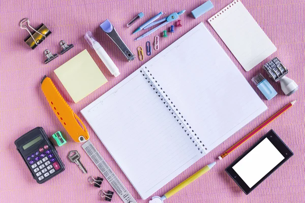 High Angle View of Colorful School Supplies Organized by Type Around Note Book Open to Blank Page Arranged on pink fabric