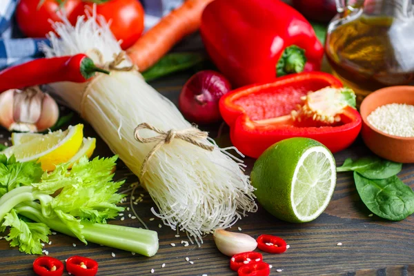 Ingredients for vegetarian noodles with vegetables - rice noodles, spinach, celery, bell pepper, carrot, tomatoes, lime, chili, sesame seeds and spices