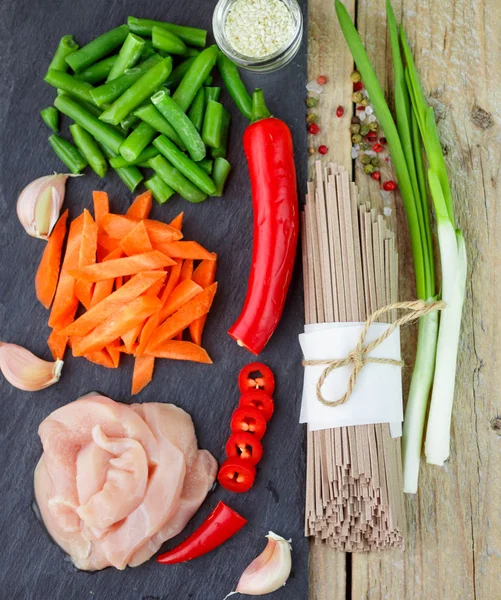 Ingredients for cooking buckwheat soba noodles with chicken and vegetables - dry raw buckwheat noodles , chicken, red pepper, green beans, carrots, garlic and green onions. Asian cuisine