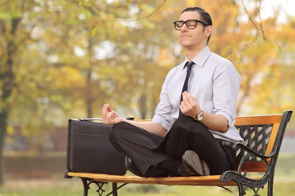 Businessman meditating seated on a bench