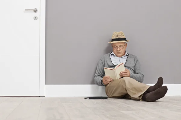 Senior gentleman reading a book seated on the floor