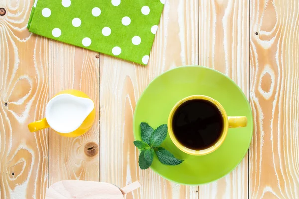 Cup of black tea on light green plate and yellow milk ju