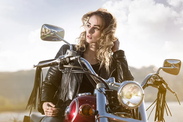 Biker girl in  leather jacket on a motorcycle looking at the sunset.