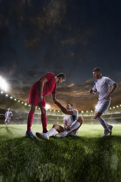 Soccer player helps onother one on sunset stadium background panorama