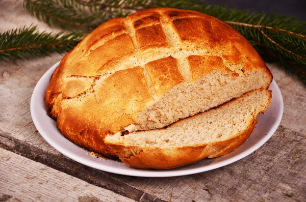 Fresh home baked bread is lying on  a wooden table with Christmas tree branch