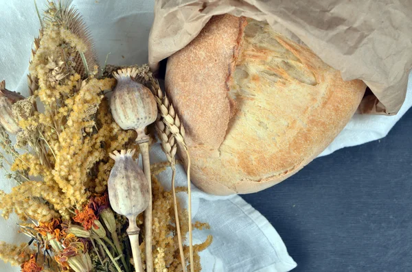 Simple healthy food. Freshly baked grain bread with sesame, vegetables, seed oil on burlap napkin with bouquet of wild flowers. Wooden planks surface