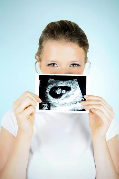 Young happy woman is hiding behind a baby scan photo.