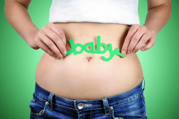 Close-up portrait of a womans stomach in early pregnancy and woman holding a green coloured word baby above her navel.