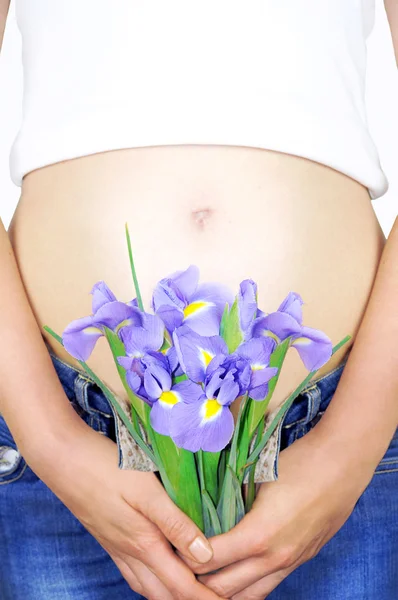 Close-up portrait of a pregnant womans baby bump in early pregnancy and purple iris flowers.