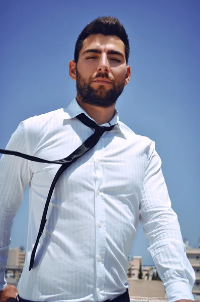 Attractive Spanish looking young man with a beard and dark hair and eyes wearing a sophisticated white shirt and a tie.