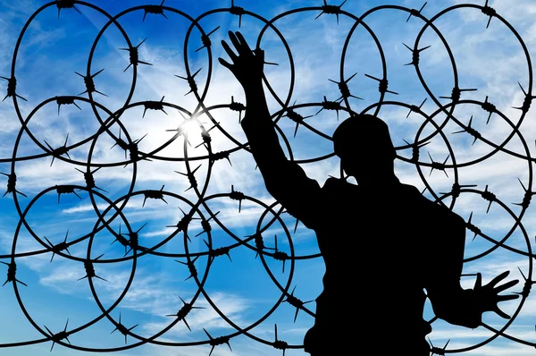 Silhouette male refugee and a barbed wire fence