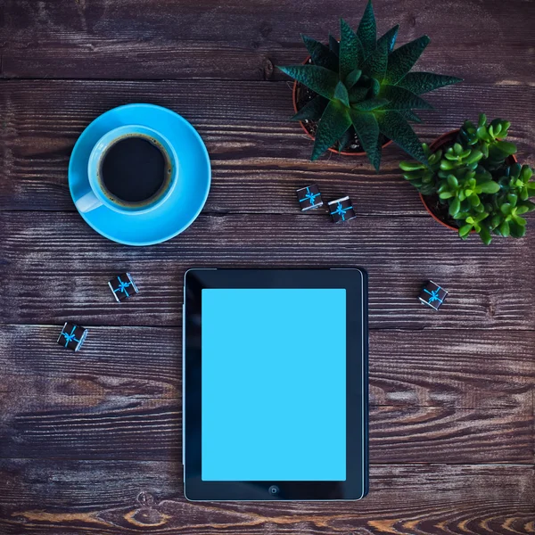 Digital tablet computer with cup of coffee and succulents on old wooden desk