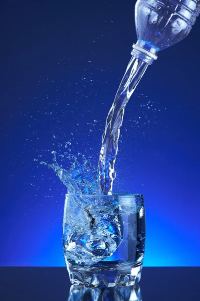 Water poured into a glass, splash, blue background, refreshing, freshness and health. Water bottle, water pitcher, blue liquid, ice, drops, motion, wave, splash, transparency blue liquid on water bottle or pitcher, ice, drops. Gradient background.