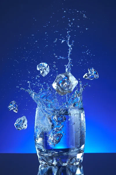 Water poured into a glass, splash, blue background, refreshing, freshness and health. Water bottle, water pitcher, blue liquid, ice, drops, motion, wave, splash, transparency blue liquid on water bottle or pitcher, ice, drops. Gradient background.