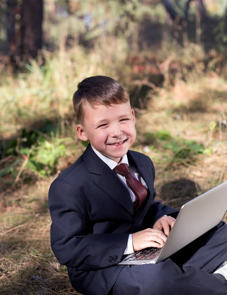 Beautiful little boy smiling while sitting with a laptop on nature