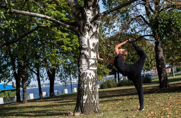 Pretty slim girl does yoga in the park. Standing at the foot of balances in the splits.