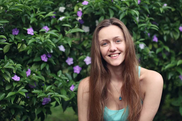 Beautiful girl with long brown hair on the background of the Bush. Girl smiling. Bush with little flowers on it.