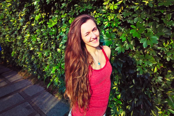 Beautiful young girl on the background of the Bush. The girl is happy and smiling . She is with long brown hair. Her face shines the sun.